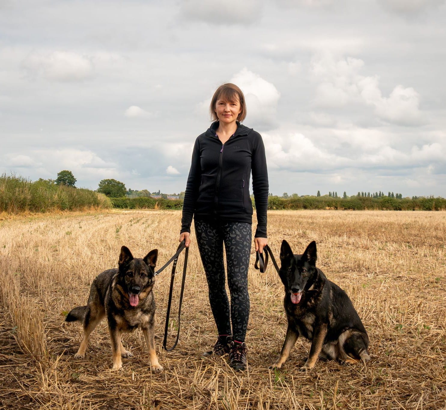 Kristine Graham with two German Shepherds in a field
